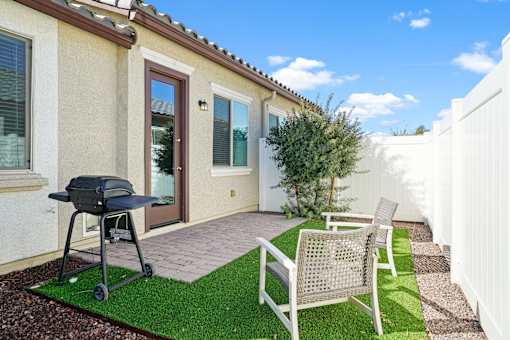 a backyard patio with a grill and two chairs at Soleil at Canyon Trails Apartments, Goodyear, 85338