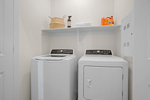 a washer and dryer in a white laundry room with a shelf above it at Soleil at Canyon Trails Apartments, Goodyear