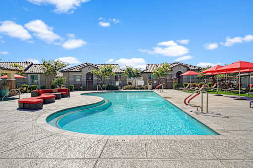 a swimming pool with red chairs and umbrellas and apartments in the background at Soleil at Canyon Trails Apartments, Goodyear, AZ, 85338