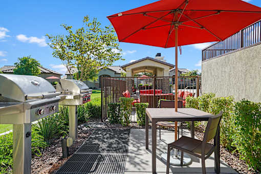 a patio with an umbrella and a table with chairs and a grill at Soleil at Canyon Trails Apartments, Goodyear, AZ, 85338