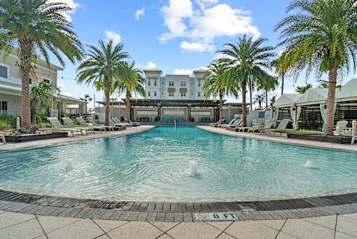 A pool surrounded by palm trees and lounge chairs. at Centre Pointe Apartments, Melbourne, Florida