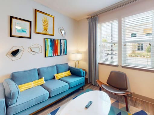 A blue couch with yellow pillows sits in a room with a white table and a chair. at Centre Pointe Apartments, Florida