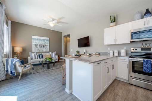 A modern kitchen with white appliances and a dining area with a couch and chairs. at Vistoria At Marley Park Apartments, Surprise, 85379