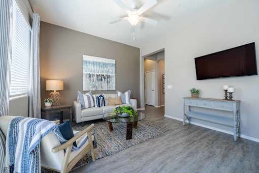 A living room with a couch, a chair, a coffee table, and a flat-screen TV mounted on the wall at Vistoria At Marley Park Apartments, Surprise, AZ, 85379