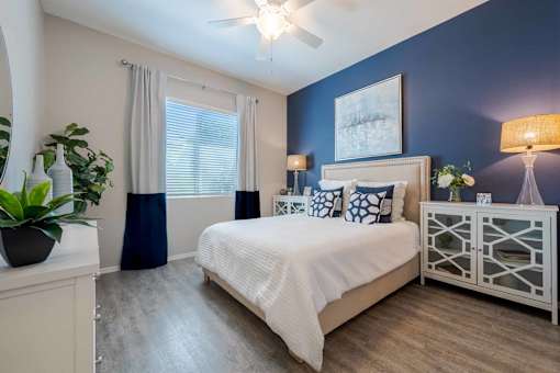 A bedroom with a bed, nightstand, and a plant. at Vistoria At Marley Park Apartments, Arizona