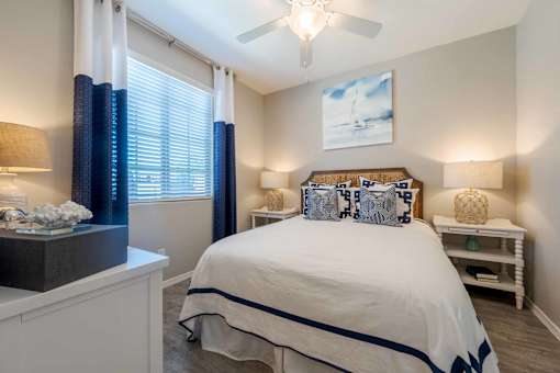 A bedroom with a bed, nightstand, and window with curtains. at Vistoria At Marley Park Apartments, Surprise, AZ, 85379