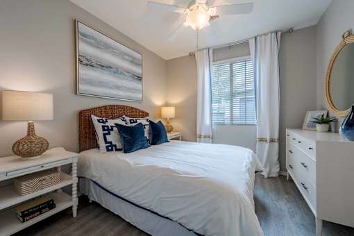 A bedroom with a large bed, a ceiling fan, and a painting on the wall.