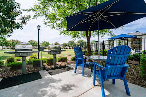 A blue chair is in front of a table with a blue umbrella. at Vistoria At Stadium Apartments, Glendale, AZ, 85305