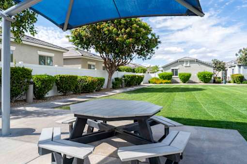 A picnic table with a blue umbrella is set up on a concrete slab. at Vistoria At Country Place Apartments, Arizona