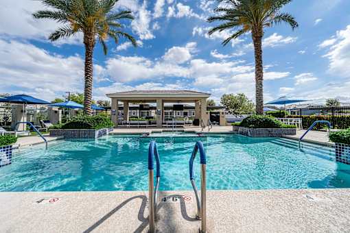 A pool surrounded by palm trees and a pavilion. at Vistoria At Country Place Apartments, Tolleson