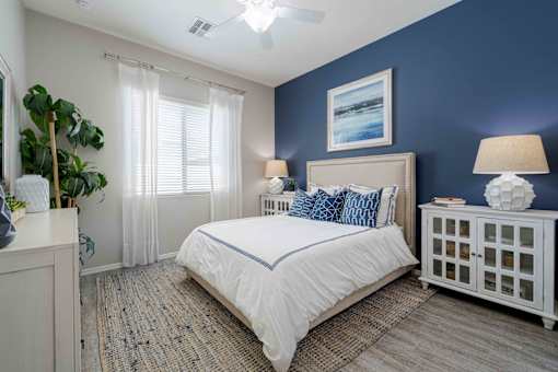 A bedroom with a large bed, a nightstand, and a window with curtains. at Vistoria At Country Place Apartments, Tolleson, AZ, 85353