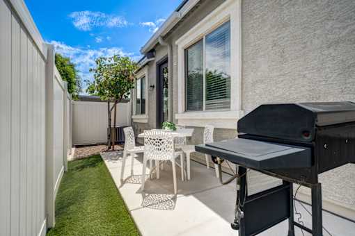 A patio with a table, chairs, and a grill.
