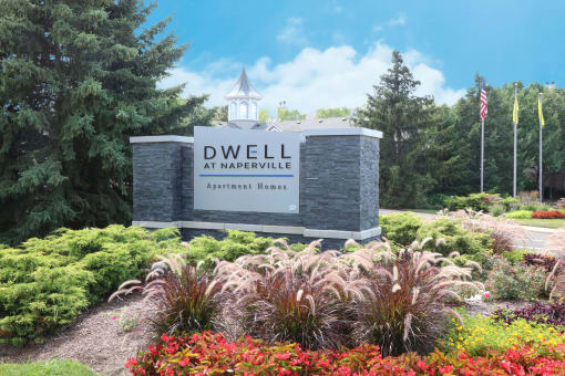 a sign at dwell at naperville entrance with flowers and trees
