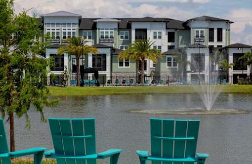 a row of green chairs in front of a lake with apartments in the background at The Addison on Long Bayou Apartments, Florida, 33772