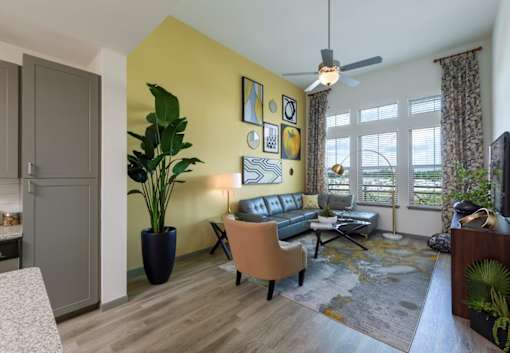 a living room with a yellow wall and a ceiling fan at The Addison on Long Bayou Apartments, Seminole, FL