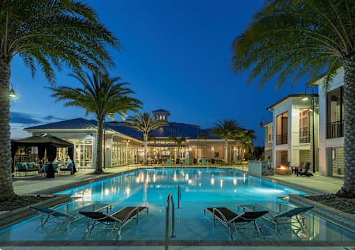 a large swimming pool in front of a hotel at night at The Addison on Long Bayou Apartments, Seminole, FL