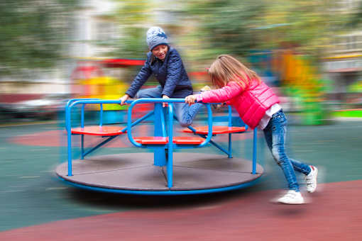 two girls playing on a merry go round on a playground