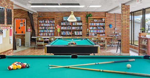 A pool table with a green cloth and a yellow cue stick.