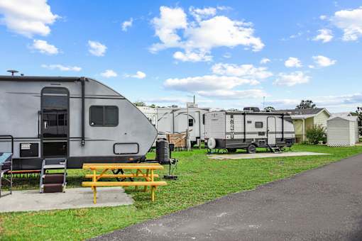 A grey RV is parked next to a picnic table.