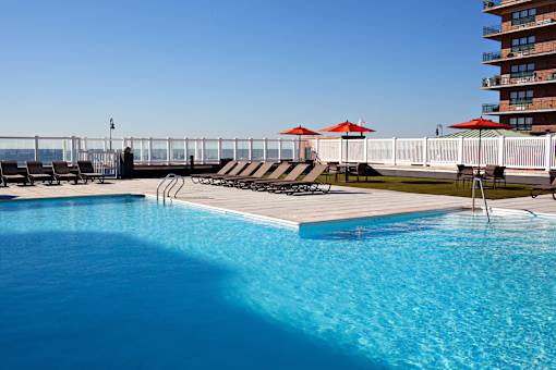 a swimming pool with chairs and umbrellas next to a hotel at 10 West Apartments, Long Beach, NY