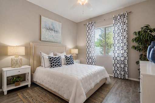 A bedroom with a large bed, a nightstand with a lamp, and a painting on the wall.