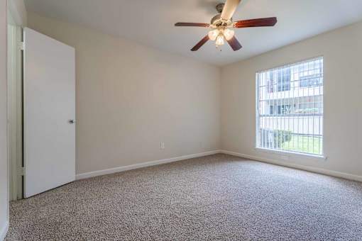 A room with a ceiling fan and a window with blinds.