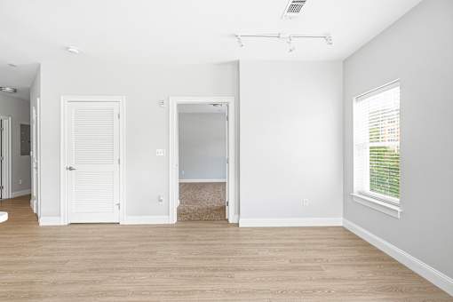 A room with a white door, a window with blinds, and a rug on the floor.