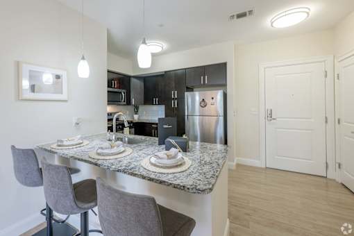 A kitchen with a granite countertop and grey chairs.