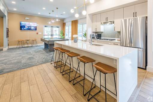 A modern kitchen with a long white counter and bar stools.