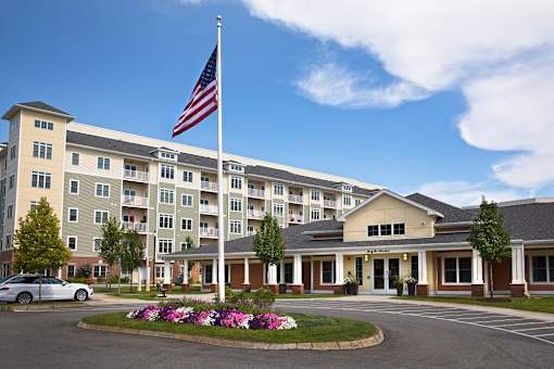 A large building with a flag on top and a flower bed in front at Axis at Lakeshore Apartments, Bridgewater, MA 02324