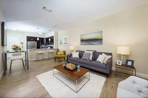 A modern living room with a grey couch, a coffee table, and a painting on the wall at Axis at Lakeshore Apartments, Massachusetts