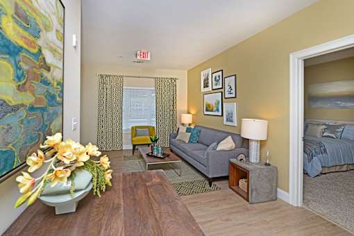 A living room with a grey couch, a coffee table, and a painting on the wall at Axis at Lakeshore Apartments, MA,02324
