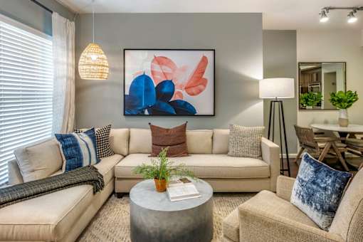 A living room with a beige couch, a grey coffee table, and a large abstract painting on the wall.