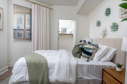 A bedroom with a bed covered in a white sheet and a green blanket.