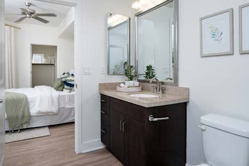 A bathroom with a white tub, a sink, a mirror, and a bedroom with a bed and a window.
