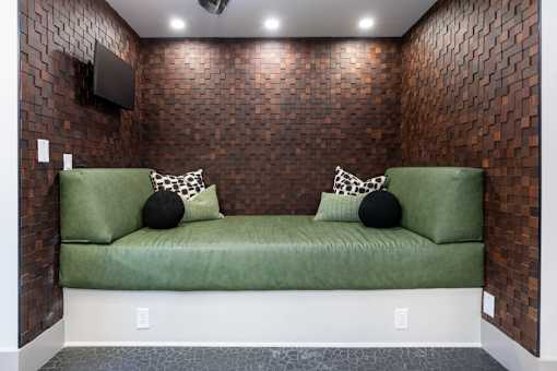 A green couch with two pillows sits against a brick wall.