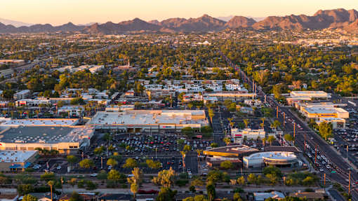 A cityscape with a large parking lot in the foreground and mountains in the background.