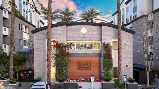 A modern building with a brown facade and a sign that reads "Level" is surrounded by palm trees and other greenery.