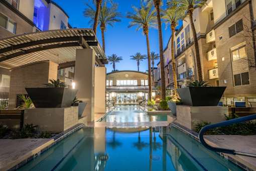 A swimming pool in a courtyard surrounded by palm trees and buildings.