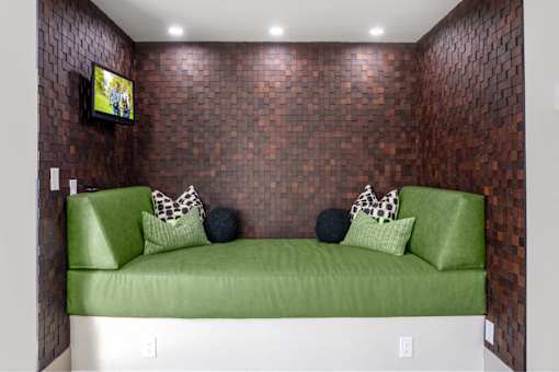 A green couch with a pillow and a TV on the wall.