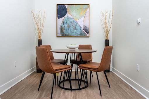 A dining table with four chairs and a painting on the wall.