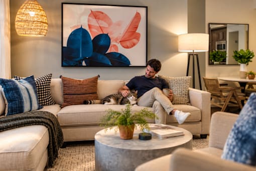 A man is sitting on a couch in a living room with a large abstract painting on the wall behind him.