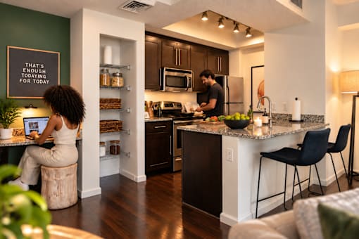 A woman is sitting at a kitchen island with a man cooking in the background.