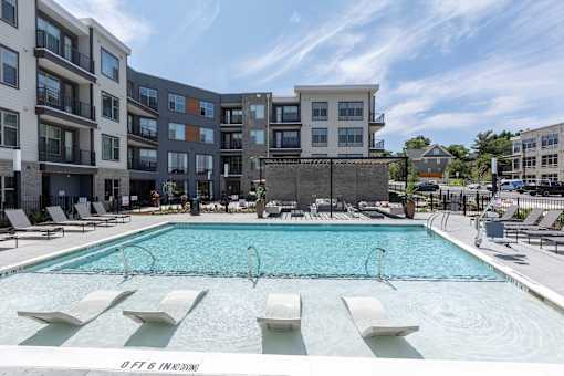 a swimming pool with lounge chairs in front of an apartment building