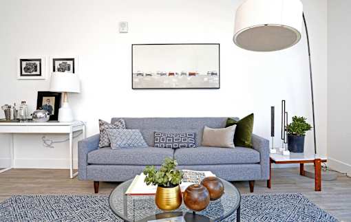 A grey couch with a glass coffee table in front of it.