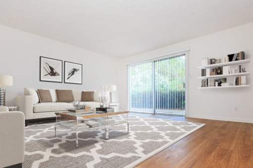 A living room with a white couch, a glass coffee table, and a rug.