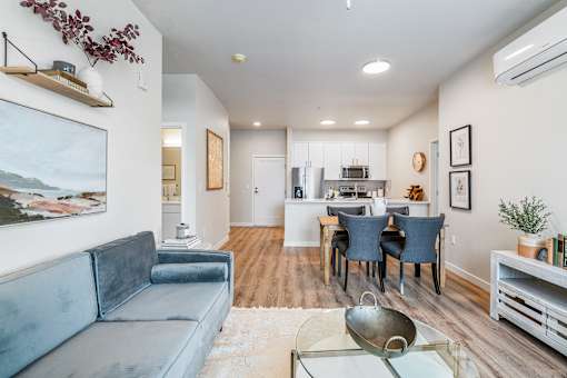 a living room with a couch a table and chairs and a kitchen in the background