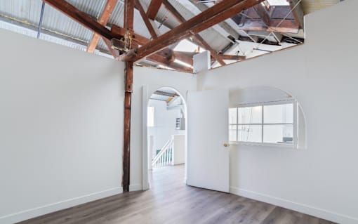 A large empty room with wooden beams on the ceiling and white walls.