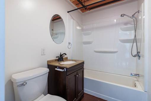 A white bathroom with a wooden vanity and a round mirror.