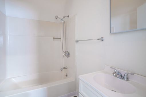 A white bathroom with a tub, sink, and mirror.